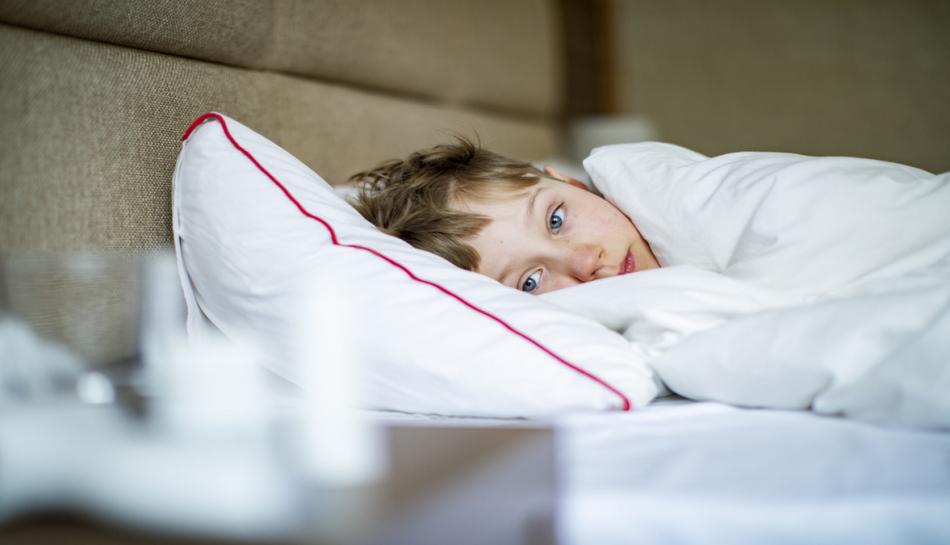 bambino a letto ammalato guarda le medicine